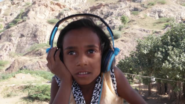 Lovely-little-Indian-listening-to-music-on-big-headphones-and-jumping-and-dancing-with-joy