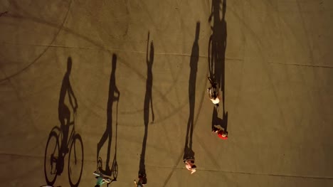 Teenagers-riding-one-by-one-on-wheeled-vehicles.-Top-view,-children-cast-long-shadows