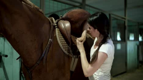 Eine-junge-Frau-befestigt-Riemen-auf-Pferdesattel