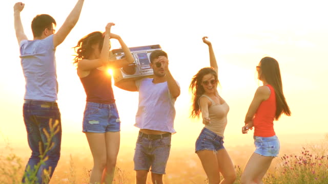 The-happy-people-with-a-boom-box-dancing-on-a-dawn-background.-slow-motion