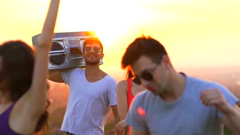 The-five-people-with-a-boom-box-dancing-on-a-sunset-background.-slow-motion