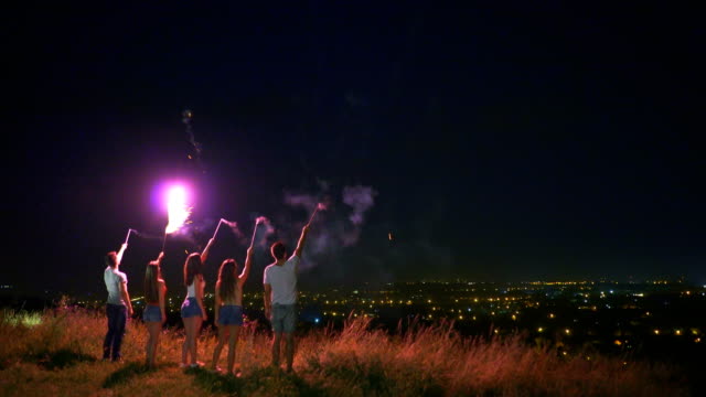 Die-fünf-Personen-halten-Sie-ein-Feuerwerk-auf-dem-Stadt-Lichter-Hintergrund-sticks.-Nachtzeit