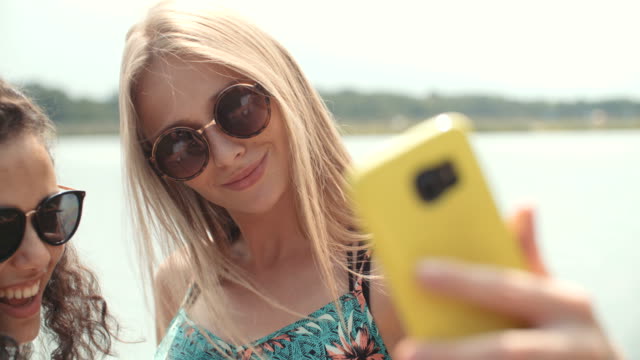 Zwei-fröhliche-Mädchen-Selfies-an-einem-See-machen.