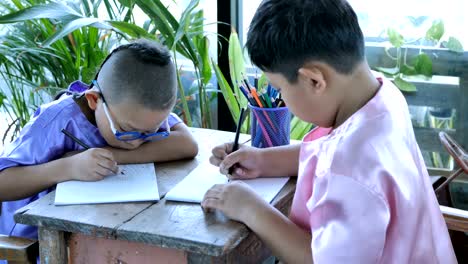Happy-little-asian-boy-with-writing-in-notebook-and-pencils-drawing-at-home.-education-concept