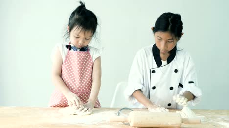 Felizes-chicas-asiáticas-con-delantal-rosado-y-uniforme-del-cocinero-están-preparando-harina-para-masa-de-galletas-o-pizza,-cámara-lenta