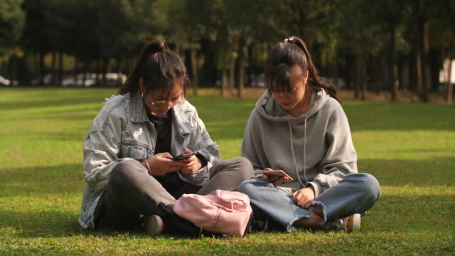 Dos-asiáticas-chica-utilizando-el-teléfono-móvil-en-el-campus