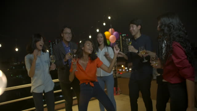 Group-of-young-friends-dancing-and-having-fun-celebrating-New-Year-and-Christmas-Festival-together-at-summer-rooftop-party.-Slow-motion.