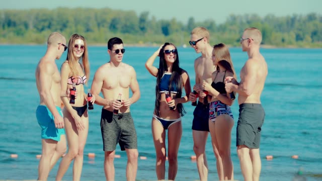 Jóvenes-amigos-felizes-en-un-semicírculo-y-comunican-en-la-playa-cerca-del-agua-con-botellas-de-refresco
