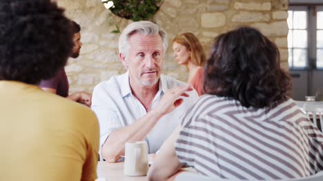 Over-shoulder-view-of-senior-man-talking-to-friends-at-table-in-a-restaurant,-waist-up