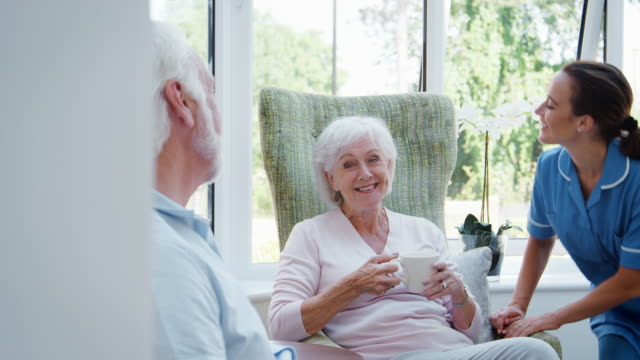 Älteres-Paar-sitzt-im-Stuhl-und-im-Gespräch-mit-der-Krankenschwester-im-Altenheim