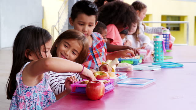 Grundschule-Kinder-sitzen-am-Tisch-mit-Lunchpaket