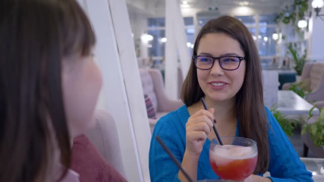 lächelnde-Freundinnen-in-Brillen-Spaß-sagen-und-trinken-Saft-durch-Stroh-während-des-Abendessens-im-Restaurant-im-Urlaub