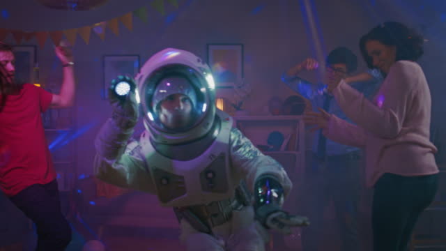 At-the-College-House-Costume-Party:-Fun-Guy-Wearing-Space-Suit-Dances-Off,-Doing-Groovy-Funky-Robot-Dance-Modern-Moves.-With-Him-Beautiful-Girls-and-Boys-Dancing-in-Neon-Lights.-In-Slow-Motion.