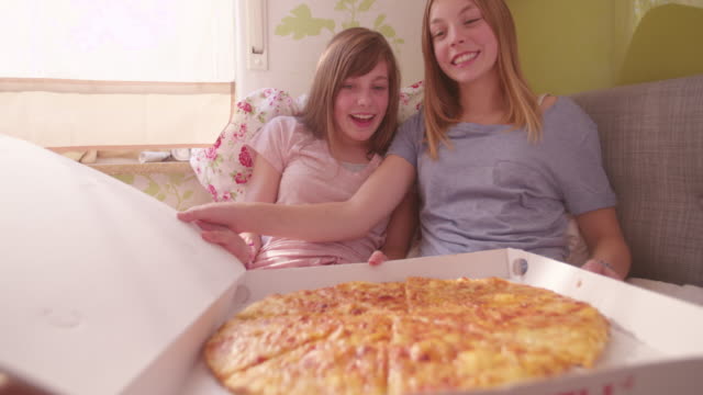 Happy-teenagers-opening-a-large-pizza-box-in-their-bedroom