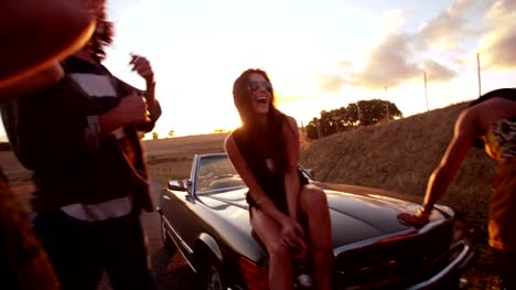 Teenage-boho-friends-sitting-on-a-convertible-hood-at-sunset