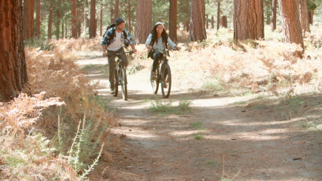 Smiling-couple-cycling-through-a-forest-together,-close-up