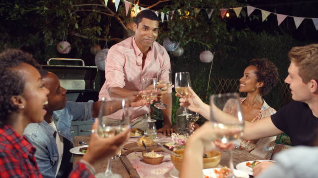 Young-man-stands-to-make-a-toast-at-an-outdoor-dinner-party