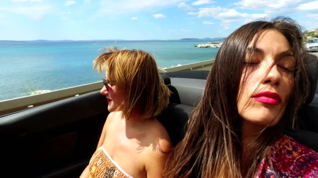 Zwei-attraktive-Frauen-reiten-auf-dem-windigen-Rücksitz-Cabrio