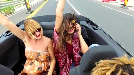 Two-beautiful-young-women-raising-their-arms-up-while-riding-in-convertible