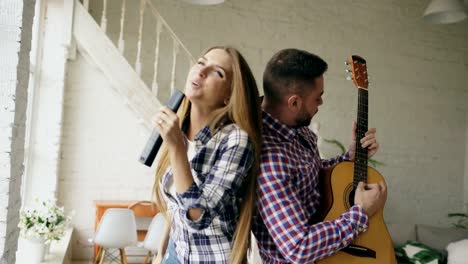 Funny-happy-and-loving-couple-dance-singing-with-tv-controller-and-playing-guitar.-Man-and-woman-have-fun-during-their-holiday-at-home