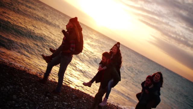 Freunde-geben-Huckepack-Fahrten-am-Strand-bei-Sonnenuntergang