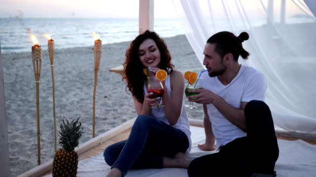 romantische-Reise,-Sommerurlaub,-Mann-und-Mädchen-in-weißen-Bungalow-am-Strand-Resort-ruhen,-junge-Menschen-in-der-Liebe-zu-bunten-Cocktails-trinken