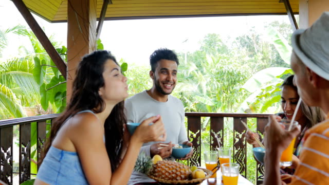 Personas-comiendo-fideos-hablando,-grupo-de-amigos-sentarse-en-mesa-en-terraza-con-vista-a-Bosque-Tropical