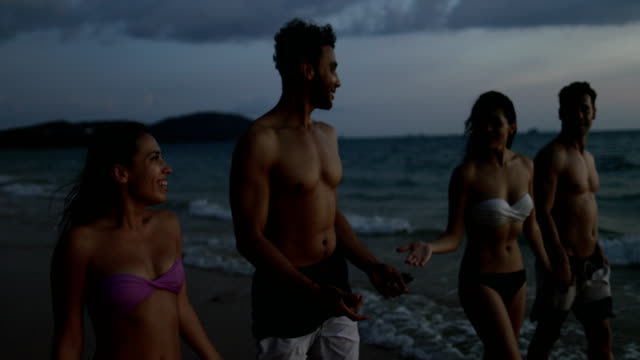 Feliz-grupo-de-amigos-caminando-en-la-playa-al-atardecer-POV-habla,-jóvenes-comunicando-durante-vacaciones-junto-al-mar