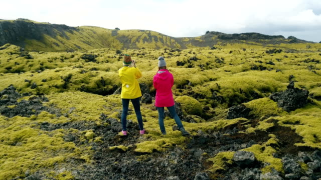 Aerial-view-of-two-woman-standing-on-the-lava-field-in-Iceland-and-enjoying-the-landscape.-Tourists-after-hiking