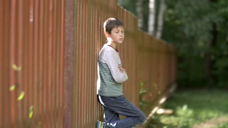 bad-serious-boy-stands-near-a-wooden-fence-and-looks-into-the-camera,-anger-in-the-boy's-eyes,-village,-nature