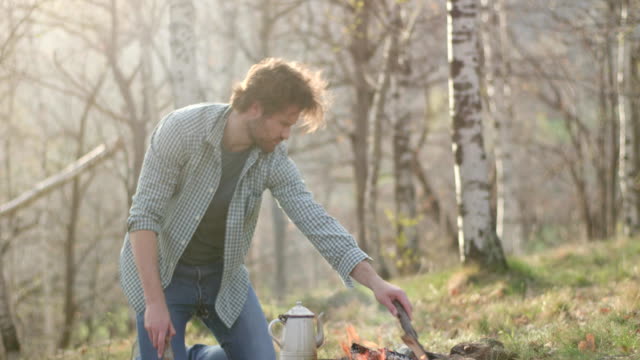 Man-lighting-fire-place-putting-wood-logs.real-friends-people-outdoor-camping-tent-vacation-in-autumn-trip.Fall-sunny-day-in-nature,-togetherness-and-friendship.-4k-video