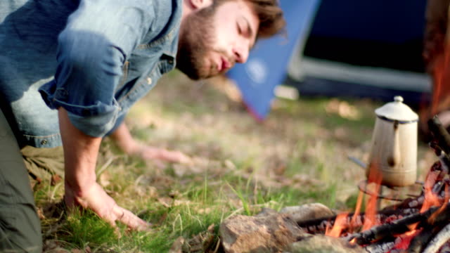 Man-lighting-fire-place-blowing.real-friends-people-outdoor-camping-tent-vacation-in-autumn-trip.Fall-sunny-day-in-nature,-togetherness-and-friendship.-4k-video