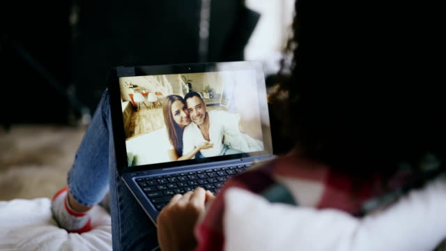 Lockige-junge-Frau,-die-mit-video-Chat-mit-Freunden-über-Laptop-Kamera-auf-Bett-liegend