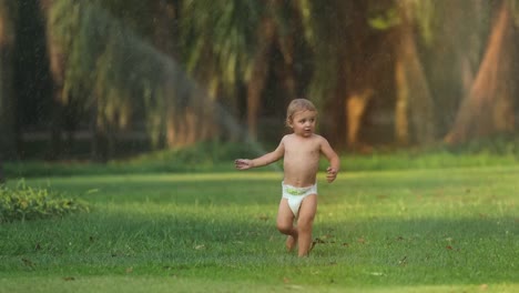 Beautiful-scene-of-infant-toddler-baby-running-in-green-field-with-water-sprinkles-during-sunset-golden-hour-time-in-4k-clip-resolution.-Slow-motion-60fps-of-infant-running-beautiful-candid-moment-in-4k
