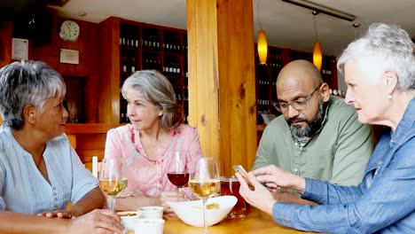 Senior-friends-using-mobile-phone-while-having-wine-4k