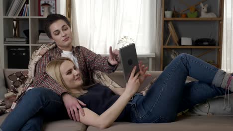 Lesbian-couple-is-resting-on-the-couch,-using-tablet-computer,-speaking,-family-idyll-60-fps