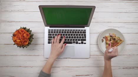 Girl-working-on-laptop-eating-pizza.-Top-view.-Hands-close-up-view
