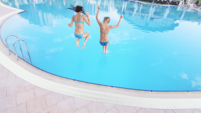 Two-girls-jump-in-swimming-pool-wide-shot