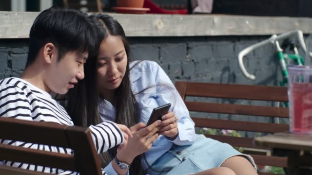 Asiatische-Teenager-Paar-mit-Smartphone-und-Lachen-im-freien