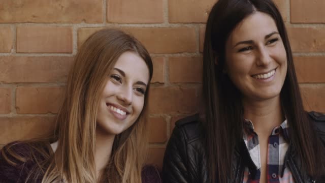 two-beautiful-women-in-front-of-brick-wall-smiling.-shot-in-slow-motion
