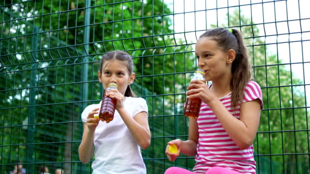 Zwei-kaukasischen-Kinder-sagen,-Geheimnisse,-lachen-und-trinken-im-Park,-im-Freien.
