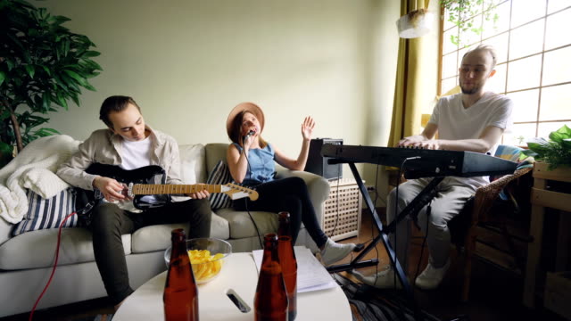 Zwei-fröhliche-Jungs-Musiker-spielen-Keyboard-und-Gitarre,-während-ihre-Freundin-Sängerin-Holding-Mikrofon-singt.-Freundschaft-und-Musik-Konzept.