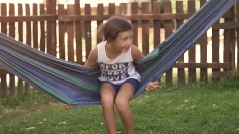 Young-happy-little-girls-in-summer-camp-lying-in-colorful-hammocks-relaxing-playing-outside-with-plushes-dog-dolls-in-green-grass-field-kids-children-slow-motion