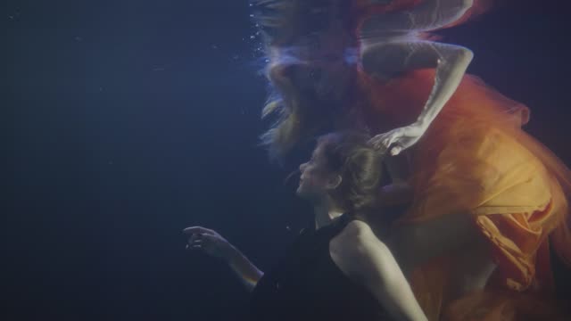 Frau-Freundinnen-in-Chiffon-Kleid-zusammen-Schwimmen-Unterwasser-auf-dunklem-Hintergrund