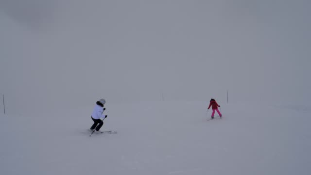 Two-Female-Skiers-Skiing-On-The-Mountain-Downhill-In-Winter-In-Heavy-Fog