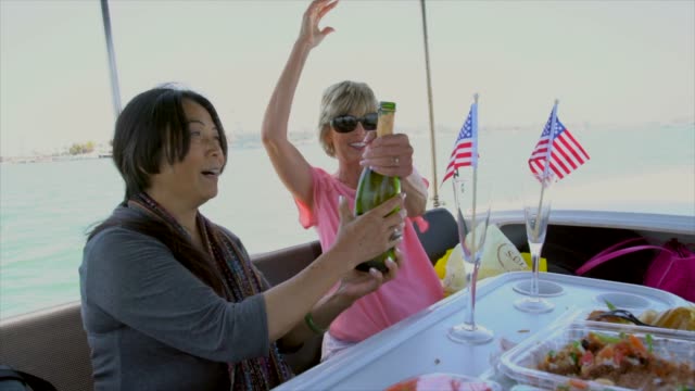 gemischtrassig-ältere-Frauen-öffnen-Champagner-und-feiern-auf-einem-Schiff