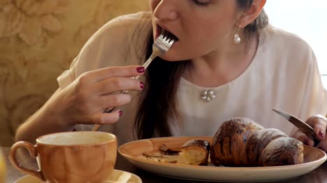 Brünette-Frau-Essen-ein-Croissant-und-Gesang-Kaffee-in-einem-café