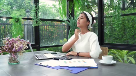 Hermosa-joven-sonriente-mujer-asiática-trabajando-en-ordenador-portátil-mientras-está-sentado-en-la-sala-de-estar-en-casa.-Mujer-de-negocios-asiática-de-trabajo-finanzas-documentos-y-calculadora-en-su-oficina-en-casa.-Disfrutando-en-casa.