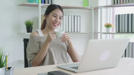 Attractive-young-asian-woman-smiling-positive-and-drinking-coffee-break-feeling-relax-and-calm-at-home-office.