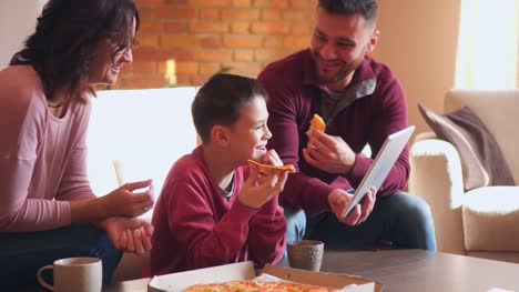 Familia-feliz-con-tableta-digital-mientras-comen-pizza-en-sala-de-estar